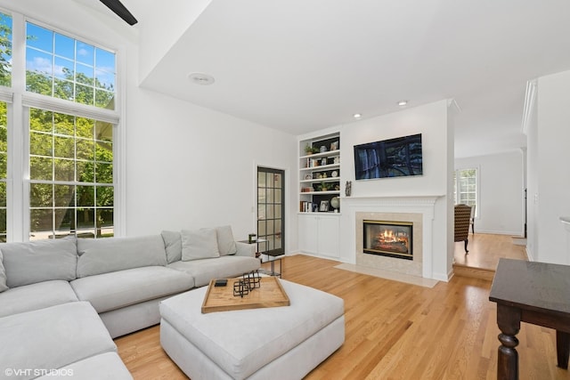 living area with healthy amount of natural light, built in features, a tile fireplace, light wood finished floors, and recessed lighting