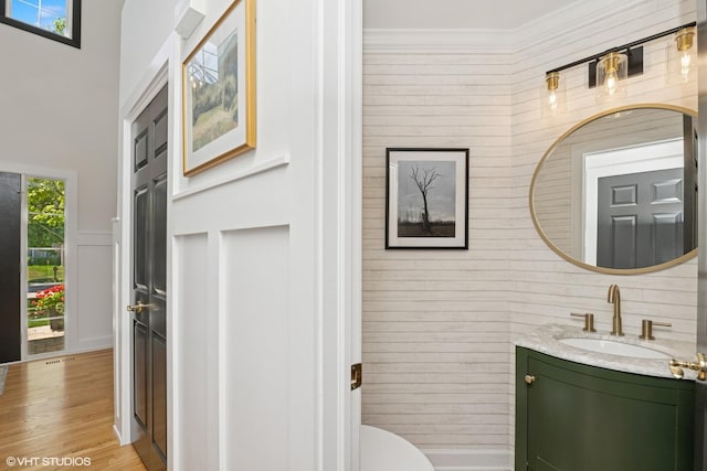 half bathroom with vanity, wood finished floors, wood walls, and crown molding