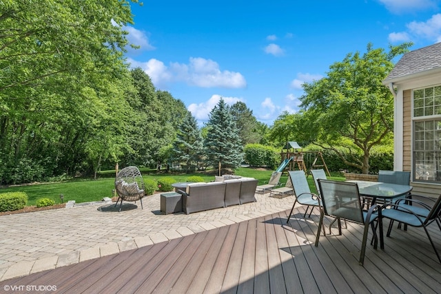 wooden deck featuring an outdoor living space, a playground, a lawn, outdoor dining area, and view of wooded area