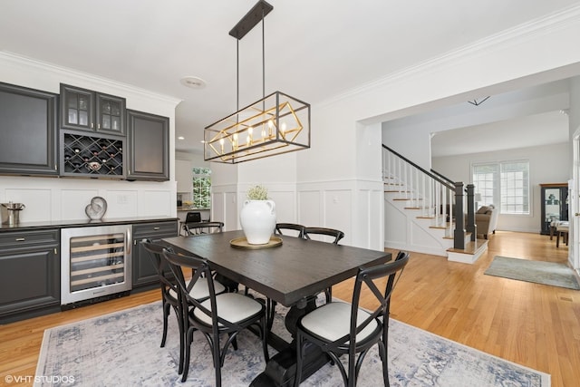 dining area with beverage cooler, a dry bar, stairway, light wood finished floors, and ornamental molding