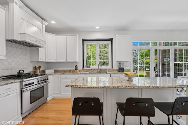 kitchen with high end stainless steel range, a breakfast bar, healthy amount of natural light, white cabinetry, and recessed lighting