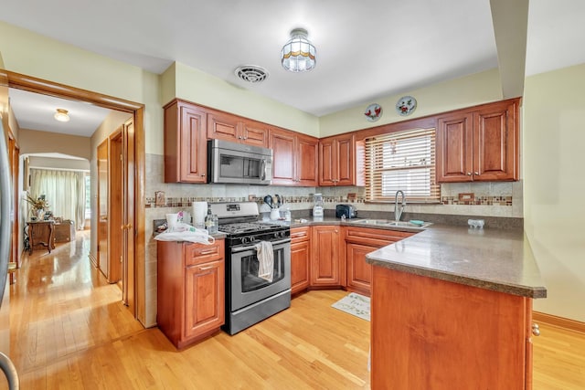 4512 S Trumbull Ave, Chicago, IL 60632 - kitchen with appliances with stainless steel finishes, a peninsula, light wood-style flooring, tasteful backsplash, and dark countertops