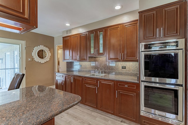 711 E Greenview Rd, Itasca, IL 60143 - kitchen featuring double oven, backsplash, dark stone countertops, light wood finished floors, and glass insert cabinets