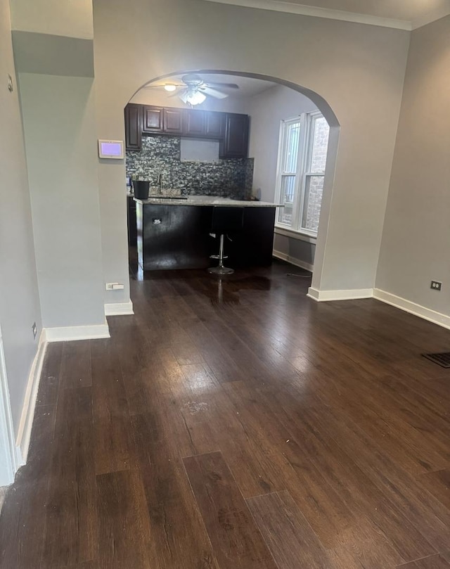 kitchen featuring dark wood finished floors, a ceiling fan, tasteful backsplash, arched walkways, and crown molding