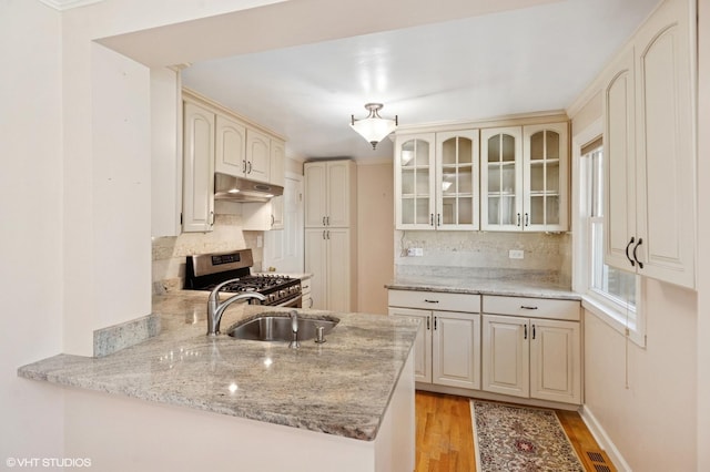 3837 Kirk St, Skokie, IL 60076 - kitchen with stainless steel range with gas stovetop, under cabinet range hood, a peninsula, glass insert cabinets, and cream cabinets