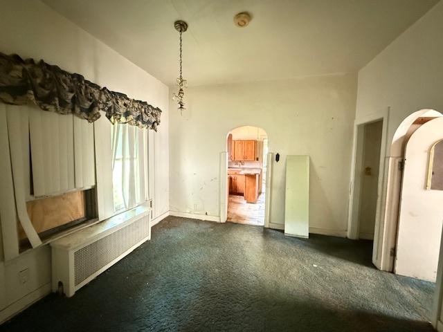 7806 S Avalon Ave, Chicago, IL 60619 - unfurnished dining area featuring radiator, dark carpet, and arched walkways