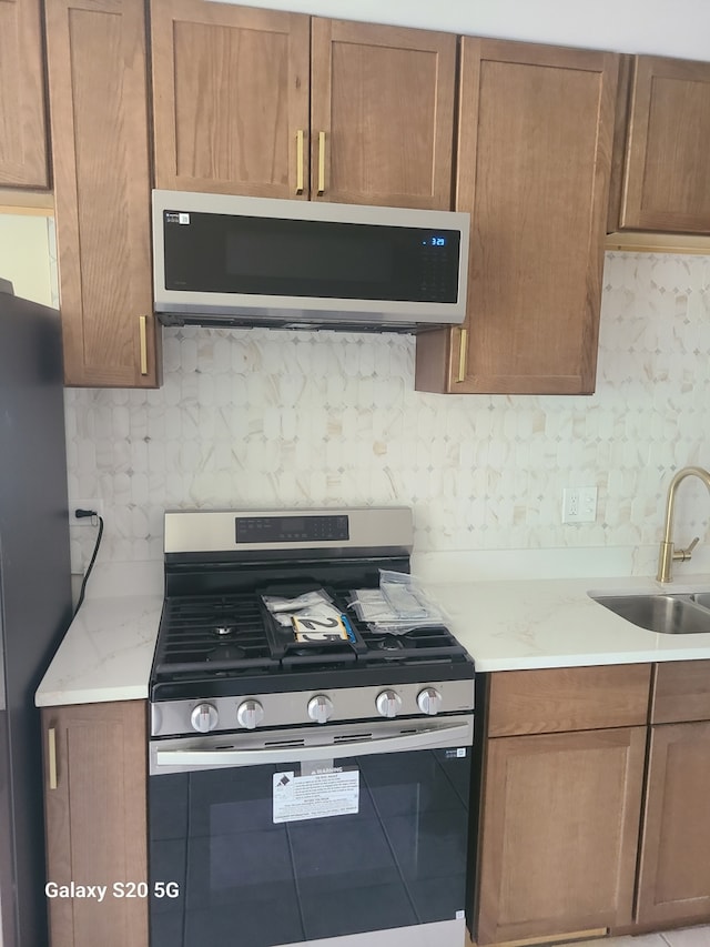 18550 Torrence Ave Unit 25, Lansing, IL 60438 - kitchen featuring stainless steel gas stove, decorative backsplash, freestanding refrigerator, and light stone counters
