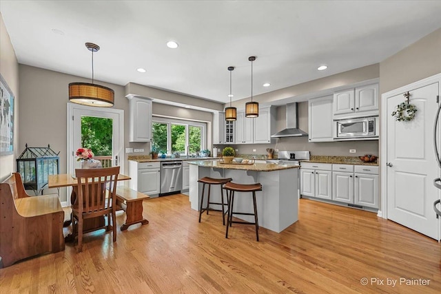 6407 Kingsbridge Dr, Cary, IL 60013 - kitchen with stainless steel appliances, wall chimney exhaust hood, light wood-style floors, a kitchen bar, and a kitchen island