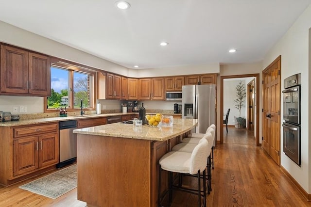 22902 W Lochanora Dr, Hawthorn Woods, IL 60047 - kitchen featuring appliances with stainless steel finishes, an island with sink, light stone countertops, wood finished floors, and a breakfast bar