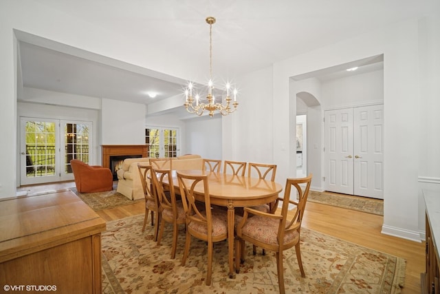 2365 Waukegan Rd Unit 2C, Northbrook, IL 60062 - dining space with light wood-style flooring, arched walkways, a chandelier, and a lit fireplace