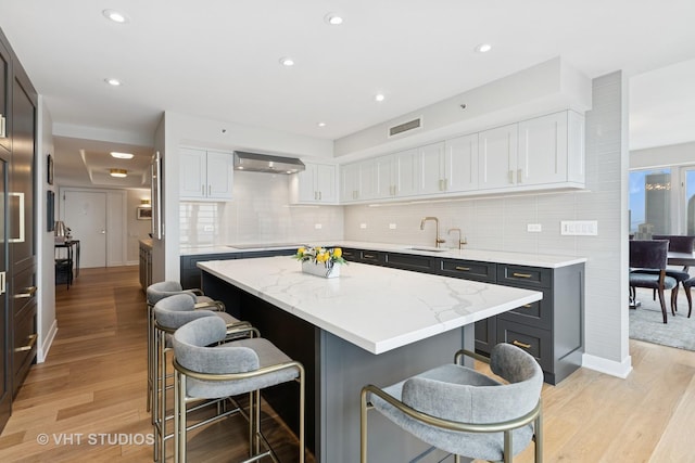 132 E Delaware Pl Unit 5101, Chicago, IL 60611 - kitchen with wall chimney exhaust hood, a breakfast bar area, white cabinetry, a kitchen island, and recessed lighting