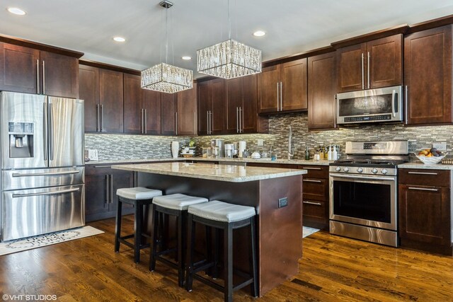 5733 S Neenah Ave, Chicago, IL 60638 - kitchen featuring appliances with stainless steel finishes, a chandelier, a kitchen island, a breakfast bar, and light stone counters