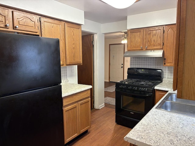 2841 10th St, Rockford, IL 61108 - kitchen featuring black appliances, under cabinet range hood, backsplash, light countertops, and wood finished floors