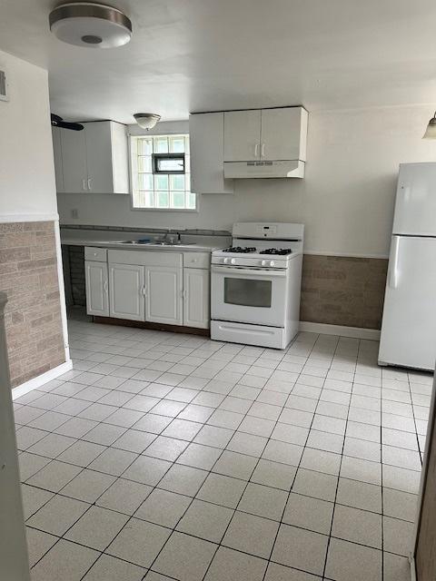 110 N Frolic Ave, Waukegan, IL 60085 - kitchen with white appliances, light tile patterned flooring, under cabinet range hood, wainscoting, and light countertops