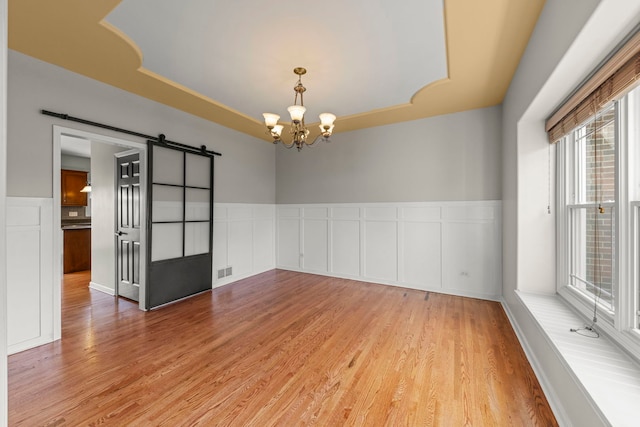 24006 Skyler Ln, Plainfield, IL 60586 - spare room featuring a barn door, a raised ceiling, light wood-style floors, a chandelier, and wainscoting