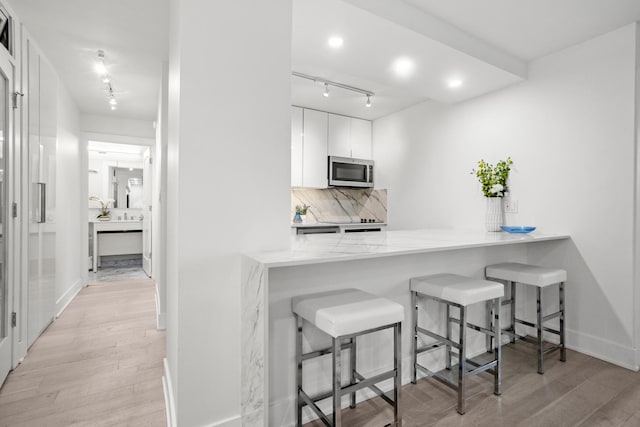 88 W Schiller St Unit 904, Chicago, IL 60610 - kitchen with stainless steel microwave, rail lighting, light wood finished floors, white cabinetry, and a breakfast bar