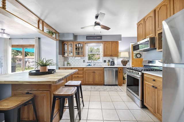 1110 N Main St, Normal, IL 61761 - kitchen featuring appliances with stainless steel finishes, wood counters, decorative backsplash, ceiling fan, and glass insert cabinets