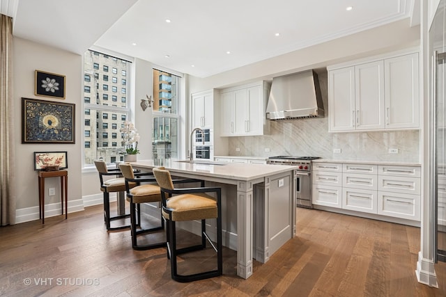 435 N Michigan Ave Unit 1203, Chicago, IL 60611 - kitchen with wall chimney range hood, high end range, a center island with sink, a breakfast bar, and hardwood / wood-style floors