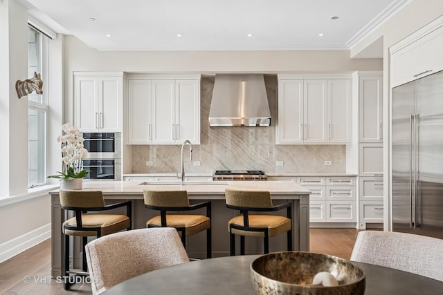 435 N Michigan Ave Unit 1203, Chicago, IL 60611 - kitchen with wall chimney exhaust hood, appliances with stainless steel finishes, light countertops, a kitchen island with sink, and crown molding