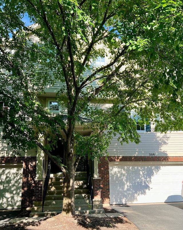 obstructed view of property with stairway, brick siding, asphalt driveway, and an attached garage