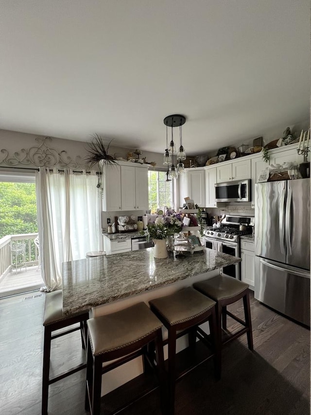 kitchen featuring stainless steel appliances, white cabinetry, a breakfast bar area, and dark stone countertops