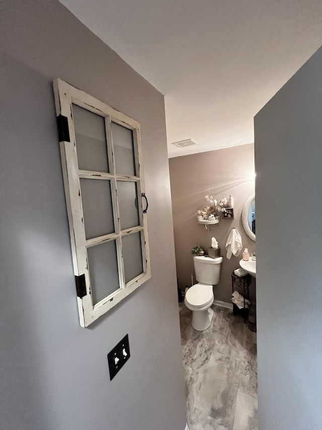 half bathroom featuring toilet and marble finish flooring