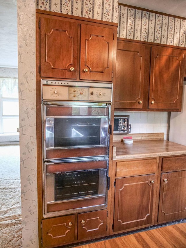 110 Hickory, Villa Grove, IL 61956 - kitchen featuring double oven, light countertops, wallpapered walls, brown cabinetry, and backsplash