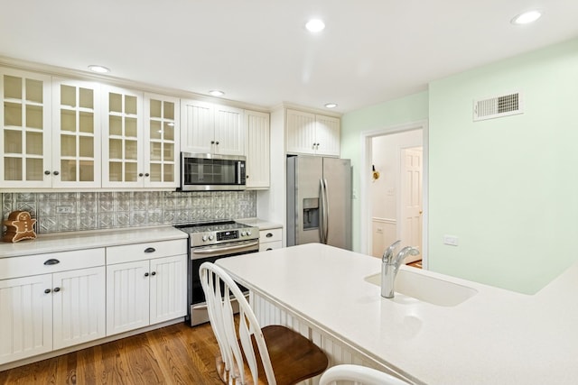 3921 Franklin Ave, Western Springs, IL 60558 - kitchen featuring appliances with stainless steel finishes, a breakfast bar area, glass insert cabinets, decorative backsplash, and light countertops