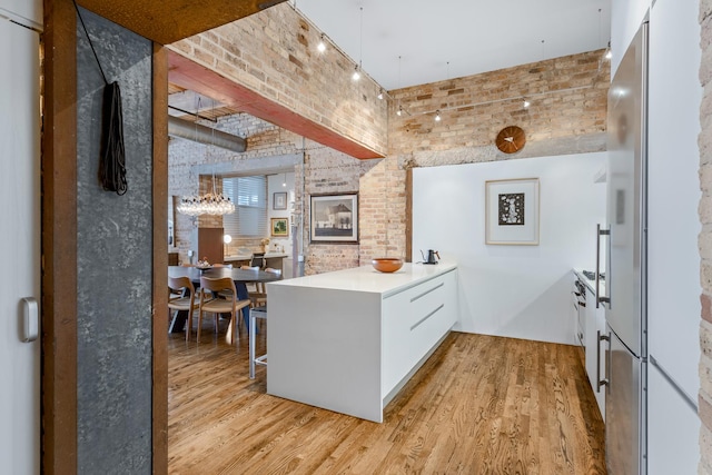 1017 W Washington Blvd Unit 2H, Chicago, IL 60607 - kitchen with light wood finished floors, a peninsula, brick wall, freestanding refrigerator, and a chandelier