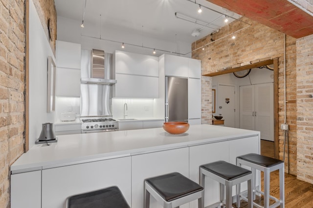 1017 W Washington Blvd Unit 2H, Chicago, IL 60607 - kitchen featuring brick wall, wall chimney range hood, white cabinets, modern cabinets, and light wood-style flooring