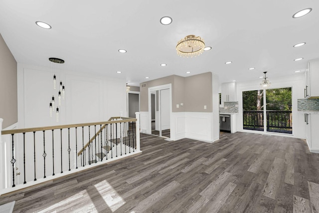 unfurnished living room featuring a decorative wall, wood finished floors, a chandelier, recessed lighting, and a wainscoted wall