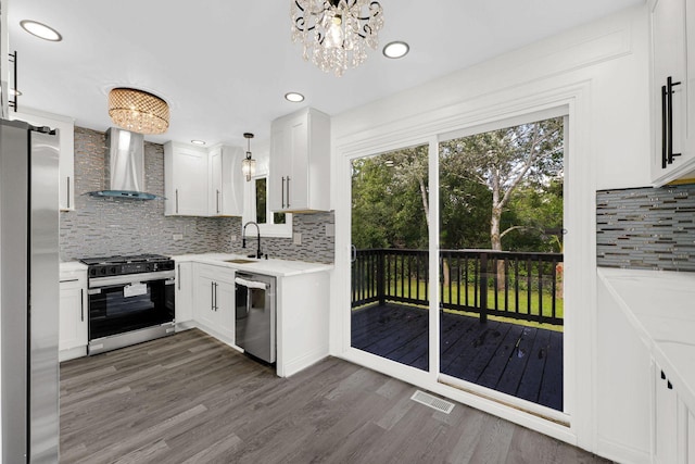 kitchen featuring wall chimney range hood, appliances with stainless steel finishes, tasteful backsplash, dark wood-type flooring, and white cabinetry