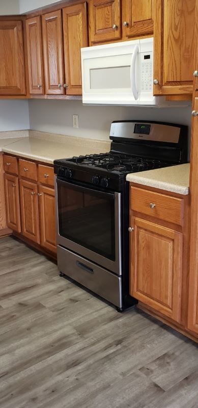 7155 W 71st St, Chicago, IL 60638 - kitchen featuring stainless steel range with gas cooktop, white microwave, brown cabinets, light wood-type flooring, and light countertops
