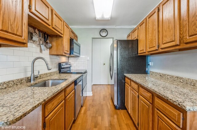 7033 N Kedzie Ave Unit 512, Chicago, IL 60645 - kitchen featuring stainless steel appliances, light wood-type flooring, decorative backsplash, brown cabinetry, and light stone countertops