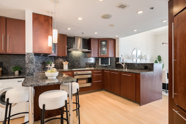950 N Michigan Ave Unit 4502, Chicago, IL 60611 - kitchen featuring stainless steel oven, wall chimney exhaust hood, a peninsula, a kitchen bar, and light wood-style floors