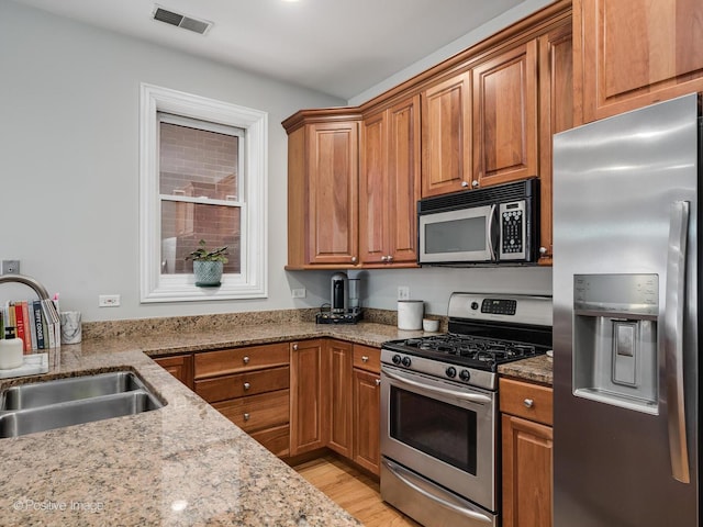 669 N Peoria St Unit 1N, Chicago, IL 60642 - kitchen with appliances with stainless steel finishes, brown cabinetry, light stone counters, and light wood-type flooring