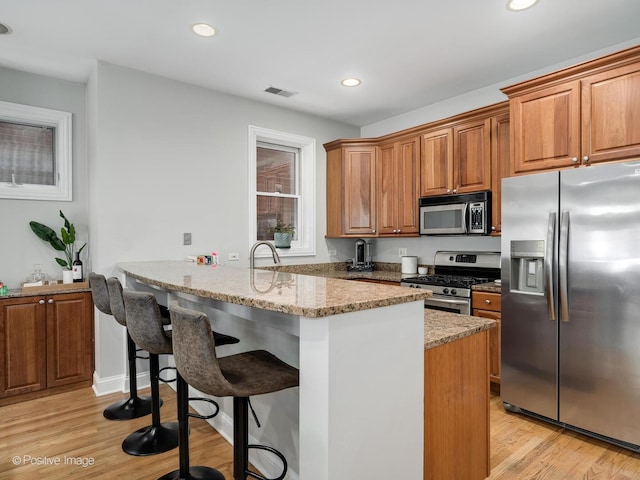 669 N Peoria St Unit 1N, Chicago, IL 60642 - kitchen featuring appliances with stainless steel finishes, a peninsula, brown cabinets, a kitchen bar, and light wood-type flooring