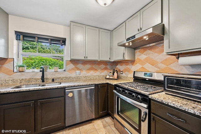 2417 Lyons St, Evanston, IL 60201 - kitchen featuring appliances with stainless steel finishes, under cabinet range hood, light stone counters, tasteful backsplash, and dark brown cabinets