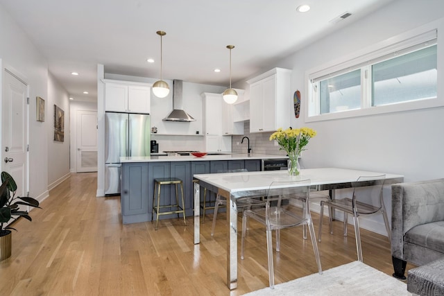 879 N Hermitage Ave Unit 2, Chicago, IL 60622 - kitchen featuring stainless steel fridge, wall chimney range hood, light wood-style floors, light countertops, and white cabinetry