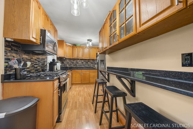 14 E Madison St, Villa Park, IL 60181 - kitchen featuring appliances with stainless steel finishes, light wood-style flooring, decorative backsplash, glass insert cabinets, and a kitchen breakfast bar