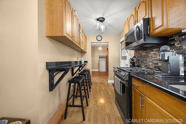 14 E Madison St, Villa Park, IL 60181 - kitchen with black gas stove, light wood-style flooring, decorative backsplash, stainless steel microwave, and a kitchen bar