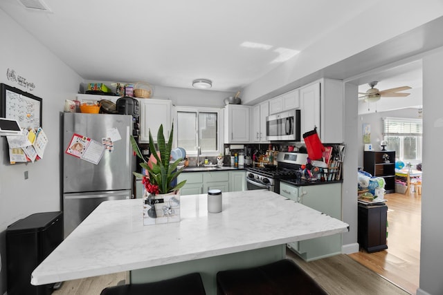 1100 Singleton Dr, Roselle, IL 60172 - kitchen with appliances with stainless steel finishes, light wood-type flooring, white cabinetry, a kitchen bar, and a ceiling fan