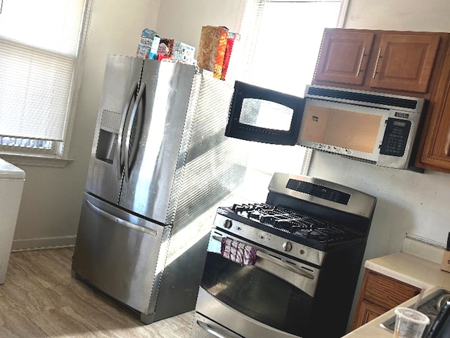 kitchen featuring stainless steel appliances, brown cabinets, light wood-style floors, and light countertops