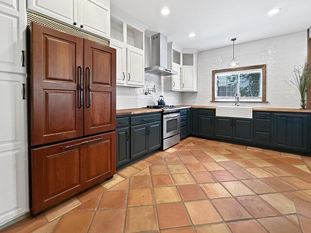 2423 Collins St, Blue Island, IL 60406 - kitchen featuring wall chimney range hood, stainless steel range with gas stovetop, paneled built in fridge, white cabinetry, and backsplash