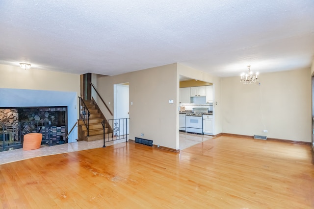 15407 Sunset Dr, Dolton, IL 60419 - unfurnished living room with a chandelier, a fireplace with flush hearth, light wood-type flooring, stairs, and a textured ceiling