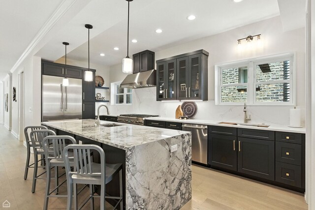 4525 N Artesian Ave, Chicago, IL 60625 - kitchen with stainless steel appliances, wall chimney exhaust hood, light stone counters, a breakfast bar area, and light wood finished floors