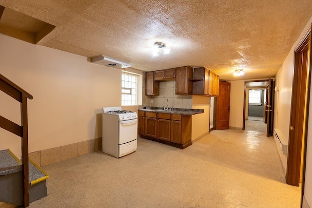 kitchen with white range with gas cooktop, brown cabinetry, a textured ceiling, decorative backsplash, and dark countertops