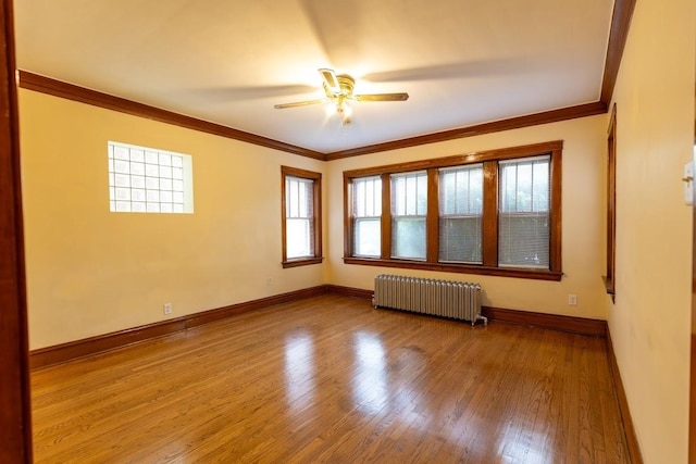 empty room with radiator, plenty of natural light, ornamental molding, a ceiling fan, and wood finished floors