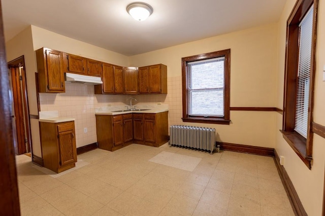 kitchen featuring radiator, under cabinet range hood, brown cabinets, and light countertops