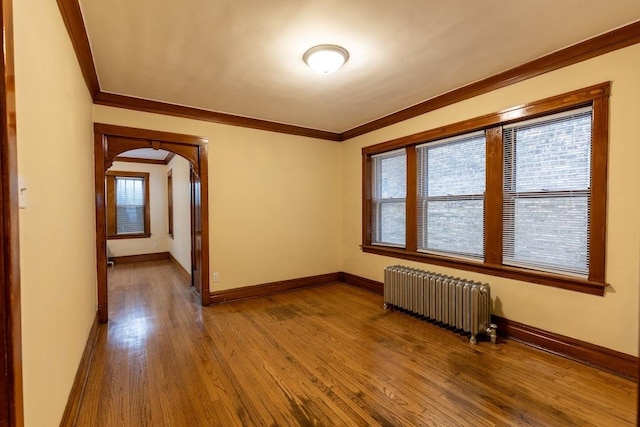 spare room with radiator heating unit, arched walkways, wood finished floors, and ornamental molding